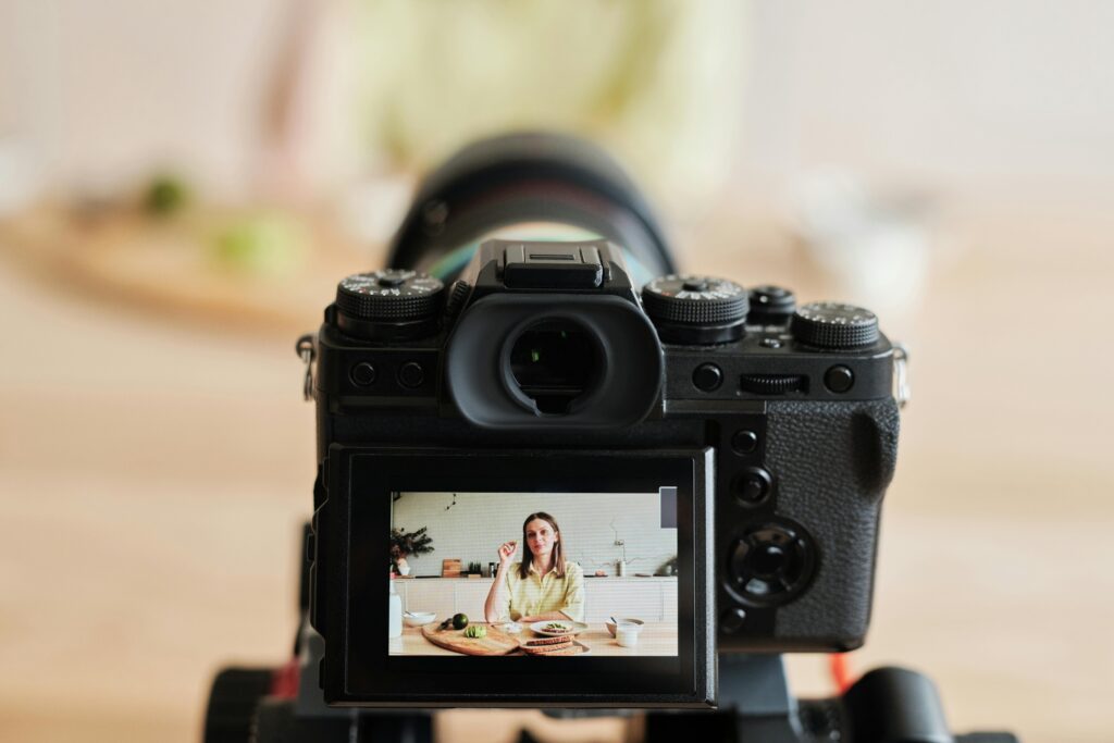 Caucasian woman vlogging at home with camera in a kitchen setting, captured indoors.